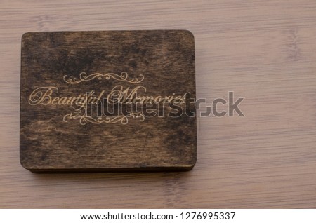 Close up of a dark wooden box on a light wooden table. A flash drive is inside the little opened box. A gift for someone to keep the memories. On the cover of the box is written ‘Beautiful Memories’.