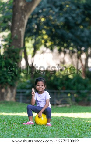 Happy Malay Girl making peace sign with her hand. Pose with football at the park. Cheeky facial expression.