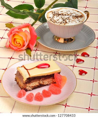 Cup of coffee, a rose and a cake on the tablecloth