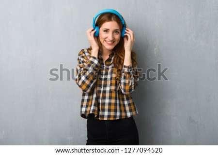 Young redhead girl over grunge wall listening to music with headphones