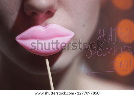 Beauty joyful Young Funny fashion model Girl holding big pink lips on a stick smiling, 8 March sign Happy Women's Day concept. On bokeh lights background.