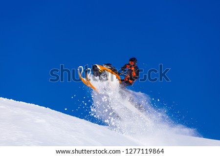 the guy is flying and jumping on a snowmobile on a background of blue sky leaving a trail of splashes of white snow. bright snowmobile and suit without brands. extra high quality  Royalty-Free Stock Photo #1277119864