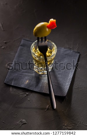 portion of Golden tequila with stuffed pepper olive on a dessert fork on a black background