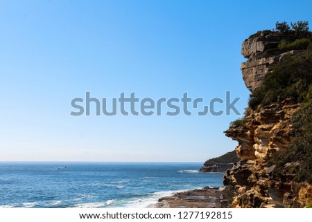 Spectacular cliffs on the Manly Beach coastal walk with waves, blue ocean / sea and a cloud-free sky in early morning hours (Sydney, Australia)