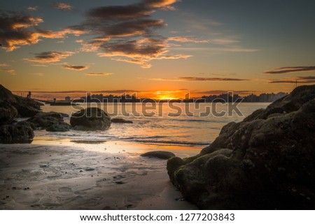 Sunset over the city, beach, cloud, submerged rock at the seashore and beautiful twilight sky