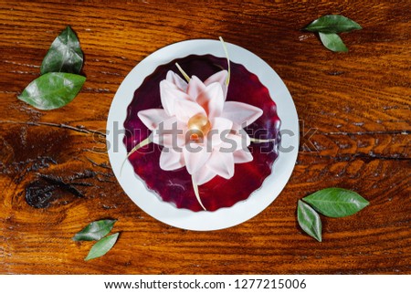 Cake with cherry glaze and pink flower on wooden table