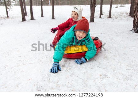 Boy and girl sliding down the hill on tubing sleds outdoors, winter day, ride down the hills, winter games and fun