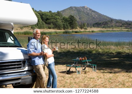Mature couple relaxing in countryside by lake on motor home vacation