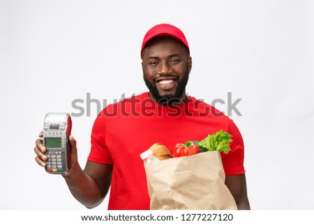 Happy young African American delivery man holding up an electronic card payment machine and delivery product. Isolated over grey background