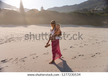 Mother in sarong walking on beach with baby daughter on vacation