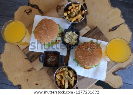 Picture two cheeseburger menus with porous, orange juice, sauces, taken from above on a table made of wood. The left is large beef cheesburger with mushrooms, while the right is a large classic cheesb
