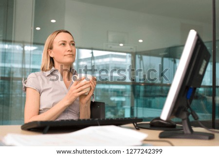 Businesswoman with computer at desk in office holding mug