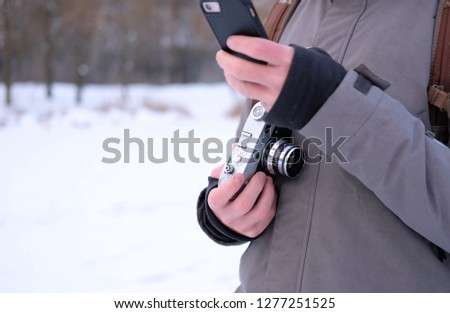 a man in a jacket holds a camera in the winter and a telephone, the theme of a winter holiday
