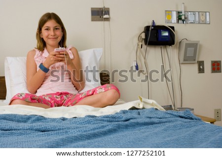 Smiling girl patient in hospital bed with MP3 player at camera
