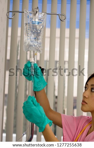 Nurse wearing gloves checking IV drip in hospital room