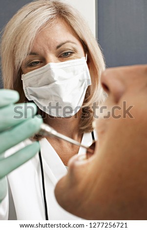 Female dentist in surgical mask giving patient dental check up using mirror