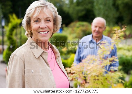 Portrait of smiling senior couple buying plants in outdoor garden center together to plant in garden