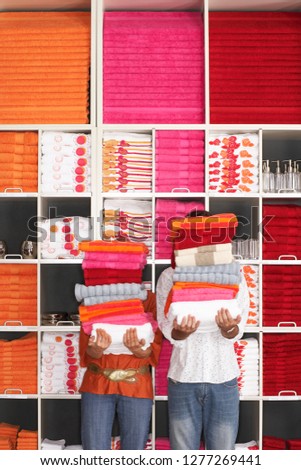 Couple homeware shopping with piles of towels in shop in front of stocked shelves