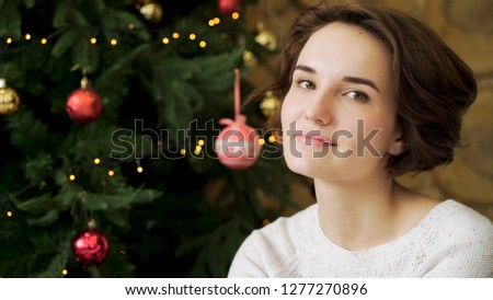 Christmas concept, beautiful brunette smiling on the background of a creatively decorated Christmas tree. Close up portrait of beautiful young woman smiling at the camera with Christmas tree behind