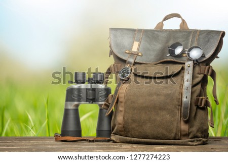 Vintage backpack, compass, sunglasses and binoculars. Tourism, travel, adventure on a natural background.