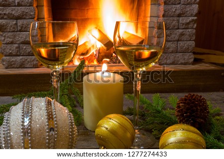 Christmas. Cozy scene before cozy fireplace with Two glasses of white wine, candle, christmas decorations- glass balls.