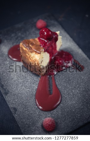 A raspberry and strawberry cheesecake slice dessert served on a rustic gray fashionable hipster slate plate. Dark food photography.