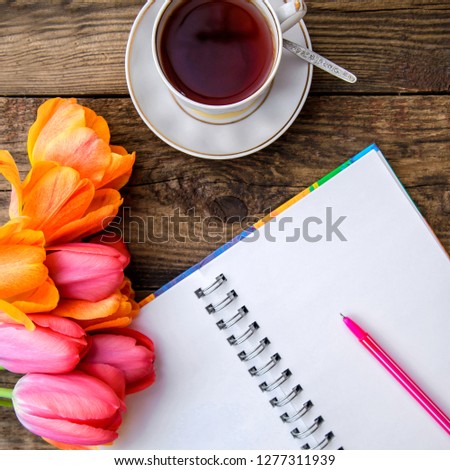 Romantic festive picture with beautiful pink and orange tulips, a cup of tea, a notebook on a wooden rustic background