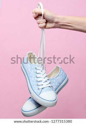 The hand holds by shoelaces retro style classic sneakers on pink pastel background. Minimalism
