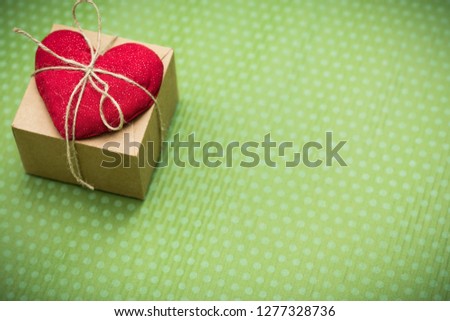 Valentine day. A red heart tied with an old thread to a gift box lies on a green polka dot background. Valentine's Day. Heart pendant. Space for text. Red heart. Eighth of March. International Women's