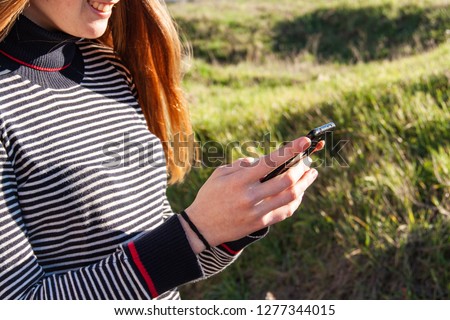 Mobile phone held in the hands of a girl, with background and green field