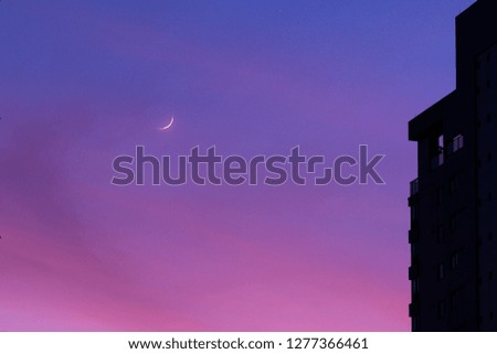 Waning moon in colourful dawn skies  and a silhouette of a part of a tall building