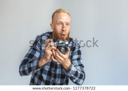 Red hair mature man standing isolated on grey wall holding film camera taking photos looking forward surprised