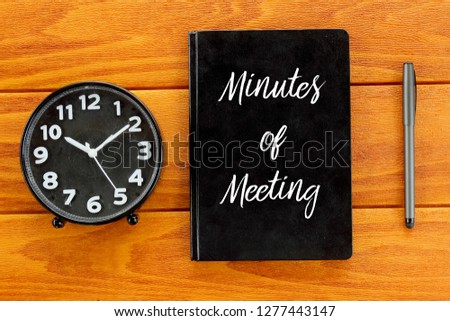 Top view of clock,pen and notebook written with Minutes of Meeting on wooden background. Business and finance concept.