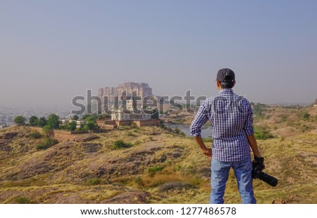 Young man in casual clothing photographing the view while standing on the hill outdoors.