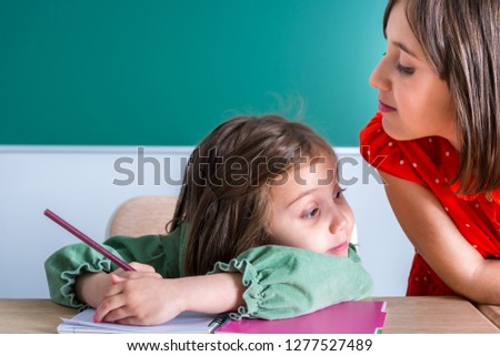 older sister looks at her younger sister as she draws in a notebook.