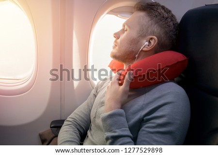 Male passenger of airplane listens to music and enjoys pillow for sleeping in chair. Concept travel Royalty-Free Stock Photo #1277529898