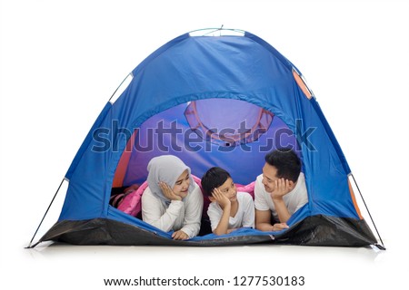Picture of young family camping in the studio while lying together in the tent, isolated on white background
