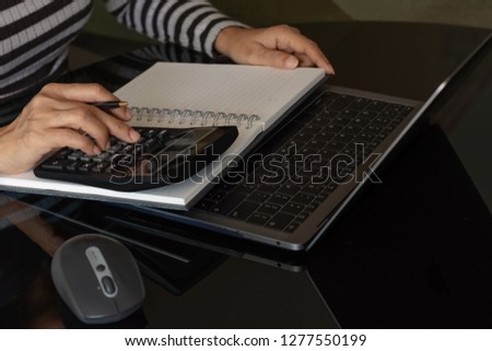 Casual businesswoman hand holding pen and using calculator to calculate business budget of company, work on laptop computer with notebook on the table. Accountant concept.  