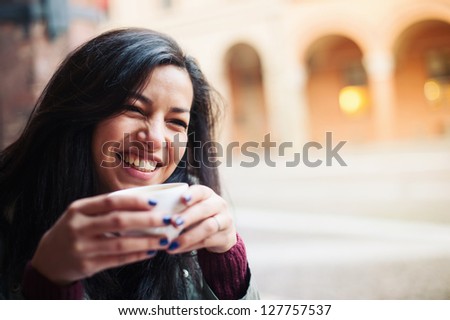 Smiling woman drinking coffee in a cafe outdoors. Shallow depth of field.