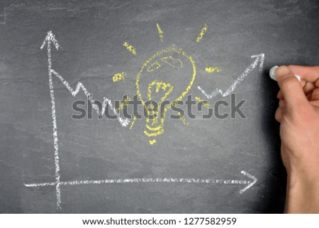 A statistical evaluation with chalk painted on a dark marble surface shows only a descending development, then a light bulb is shown which stands for the brainstorming and then the curve rises again