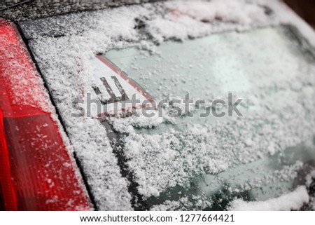 Car sticker with a Russian letter denoting spikes on a car's snow-covered rear window. The sign warns drivers that the car is equipped with spiked wheels. Safe movement on icy roads in winter