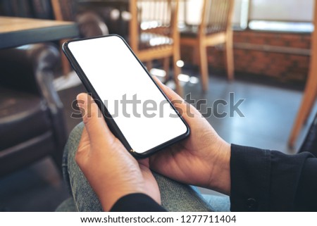 Mockup image of hands holding black mobile phone with blank white desktop screen