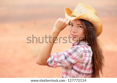 Young american cowgirl woman portrait outdoors. Beautiful natural woman saying hello looking at camera touching cowboy hat. Multicultural Caucasian / Asian girl in her twenties outdoor in nature.