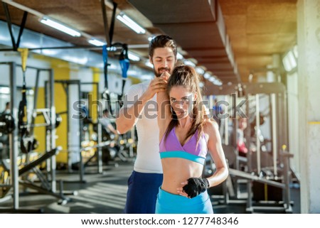 Picture of strong sporty personal trainer helping his female client to stretch her arm.Training in gym.