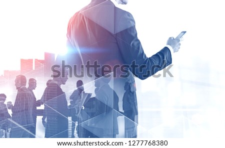 Portrait of unrecognizable businessman with smartphone and his business team members over cityscape background. Toned image double exposure