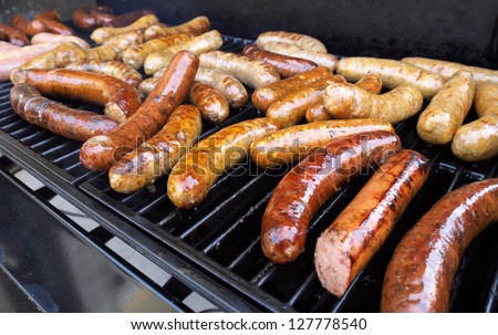 Fresh sausage and hot dogs grilling outdoors on a gas barbecue grill. Royalty-Free Stock Photo #127778540