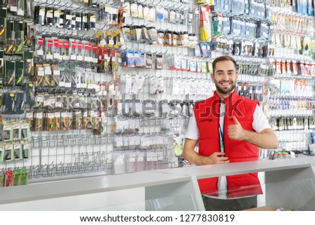 Salesman standing near showcase with fishing equipment in sports shop. Space for text