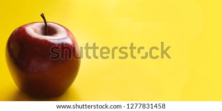 This is a close-up picture of an organic juicy red apple on a yellow background