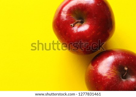 This is a close-up picture of an organic juicy red apple on a yellow background