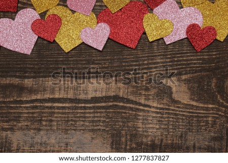 Multicolored shiny hearts on a brown wooden background. frame of hearts, top view with space for text